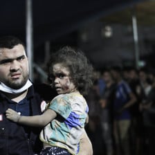 A medic wearing a face mask on his chin carries a child 