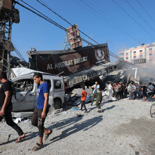 People walk past the wreckage of a bakery and a car