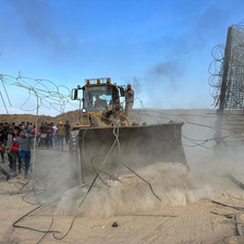 A bulldozer drives through a metal fence