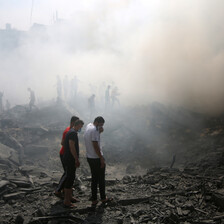 People shrouded in smoke walk through rubble