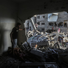 A man looks through a large hole in a building that has been attacked 