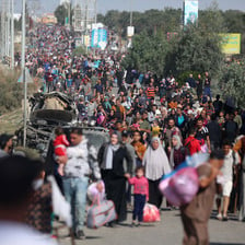 A crowd of Palestinians walking down a road and carrying their belongings stretches into the distance
