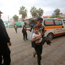 A medic carries a boy toward a hospital in Gaza. An ambulance can be seen behind the medic