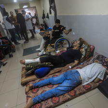 Two men lie on the ground beside a man in a wheelchair in a hospital corridor 