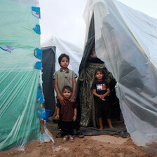 Three Palestinian children stand in between two make-shift tents of plastic