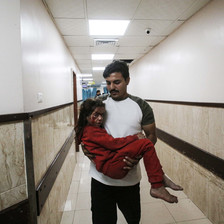 A man carries his injured daughter through a hospital corridor