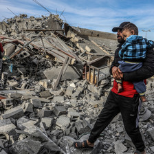 A man carries a child in what remains of a home 