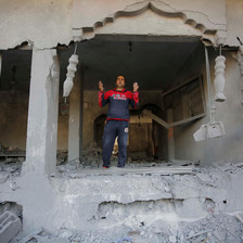 A young man wearing a dark blue tracksuit stands in what remains of a building 