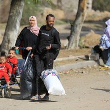 A woman pushes two girls in a pushchair as a man walks beside them carrying bags in Gaza