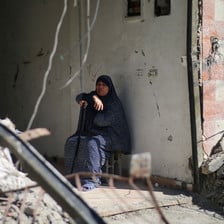 A woman sits by a wall surrounded by rubble