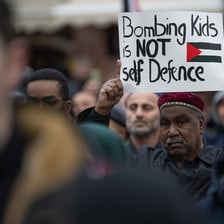 A man holds a sign reading bombing kids is not self defence