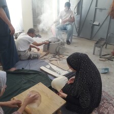 A woman shapes bread dough while a man bakes it atop an open-air oven