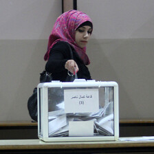 A woman casts a paper vote into a ballot box