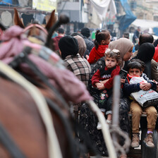 A busy street with children and horse drawn carriages