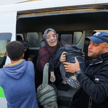 A woman is helped out of an ambulance by medics, one of whom holds an injured child