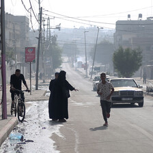 Two women walk down a nearly empty road as a young man runs past them