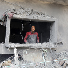 A man looks out from a glassless window of a destroyed home
