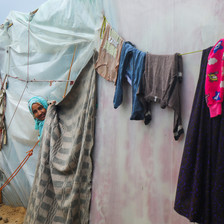 A woman smiles peeking her head out from a plastic tent, as clothing hangs on a line to dry