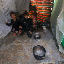 Three children sit beside pots in a makeshift tent 