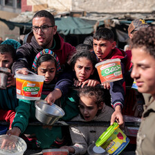 Children and some adults hold empty containers as the queue for food aid in Gaza