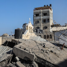 A destroyed building with a cross visible lies in ruins