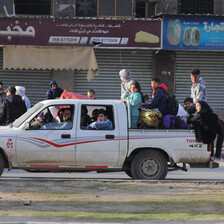 A four-door truck travels down the road, packed with people