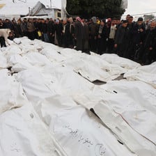 People line up at a funeral beside tens of bodies covered with white shrouds 