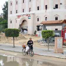 A man walks his bike in front of the wrecked facade of the Indonesian Hospital