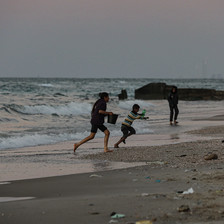 On the beach at dusk, children run from approaching waves