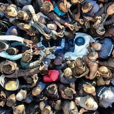 A crowd seen from above surrounds a stretcher with a press helmet