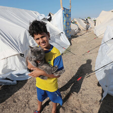 A boy holds a cat by a tent