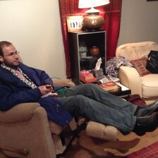 Refaat Alareer sitting in a chair in a living room which contains a lamp and a picture and some other decorations 