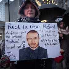 A protester holds a placard with a portrait of Refaat Alareer and a quote from his if I must die poem