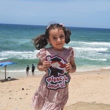 Smiling Kenzi al-Madoun, 5 years old, poses on the beach after kindergarten graduation
