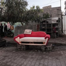 A red and white couch with heart design on the street, with a for-sale sign in Arabic