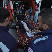 Palestinian medics wearing dark blue uniforms beside a man on a stretcher who is being taken out of an ambulance