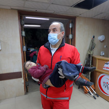 A medic wearing a mask carries an injured child in Gaza 