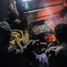 At night, a close-up of an outdoor fire and a meal being prepared by hand