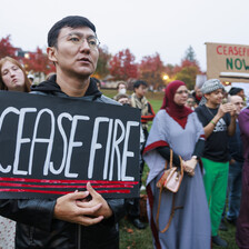 Close-up of a man holding a sign reading "ceasefire" standing on lawn with several other people