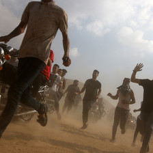 A ground view of individuals running as dirt flies in the air.