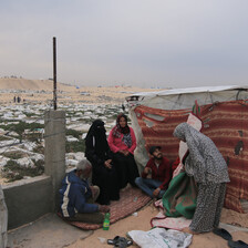 Three women and two men beside a makeshift tent next to a graveyard in Gaza