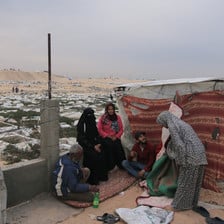 Three women and two men beside a makeshift tent next to a graveyard in Gaza 
