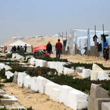 Men walk past a cemetery and tents. 