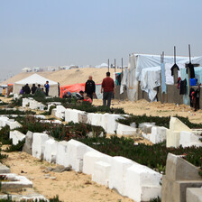 Men walk past a cemetery and tents. 