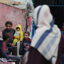 A group of children sit beside two women next to a makeshift tent in Gaza 