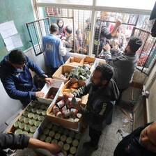 Men in a Gaza school stand beside boxes containing tinned foods as they prepare to hand them to people standing at the window