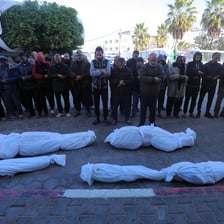 A group of mourners pray over four bodies wrapped in white body bags