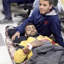 One man lies on a stretcher and another man sits beside him in a Gaza City hospital 