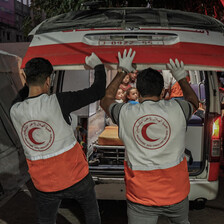 Two medics wearing vests with the logo of the Palestine Red Crescent Society prepare to close an ambulance door 