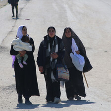 Forcibly displaced women carrying their belongings walk past Israeli forces